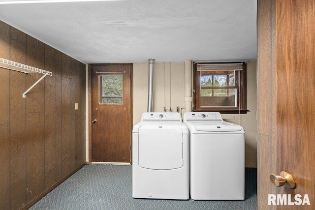 laundry room with a textured ceiling, washer and clothes dryer, and wooden walls