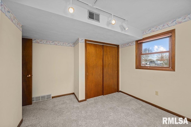 unfurnished bedroom with a closet, rail lighting, and light colored carpet