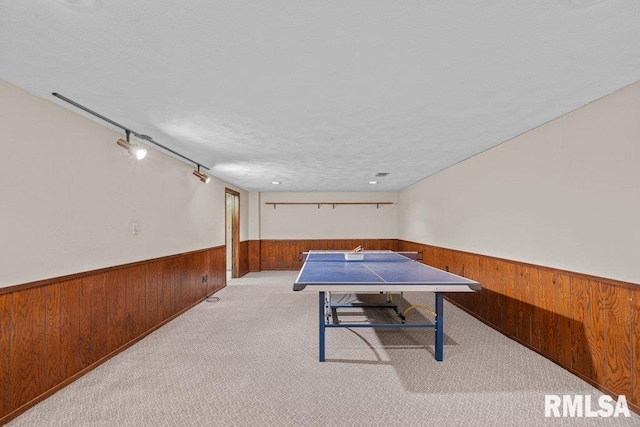 recreation room featuring a textured ceiling, light colored carpet, track lighting, and wood walls