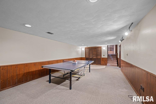 recreation room featuring a textured ceiling, light colored carpet, and wooden walls