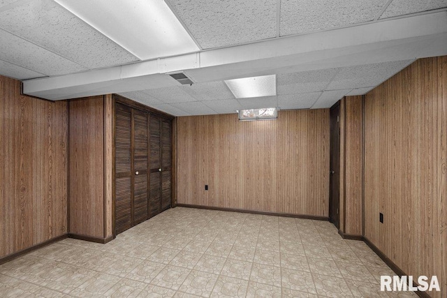 basement with wood walls and a drop ceiling