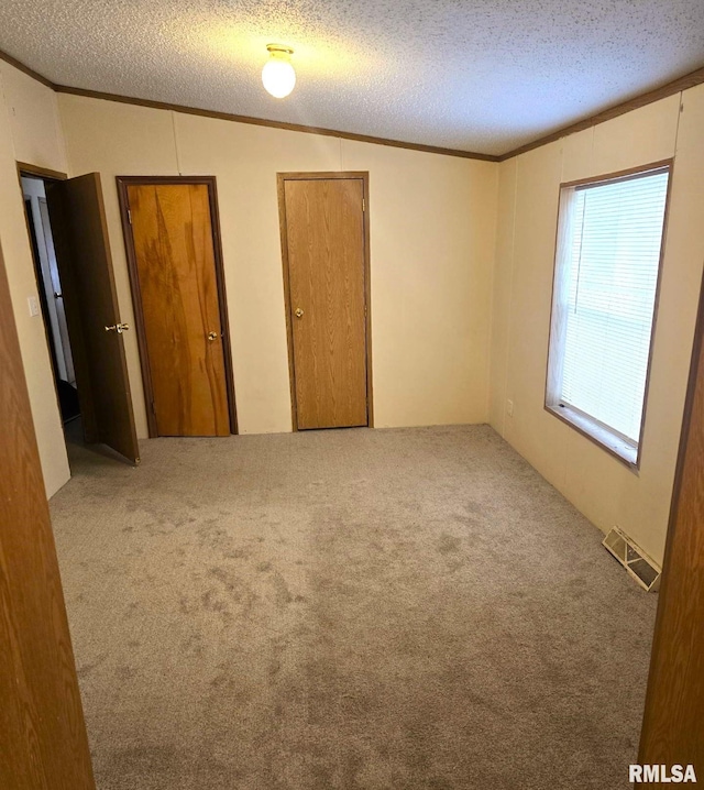 unfurnished bedroom featuring carpet, ornamental molding, a textured ceiling, and vaulted ceiling