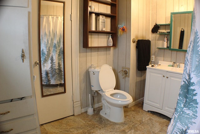 bathroom featuring toilet, vanity, and wooden walls