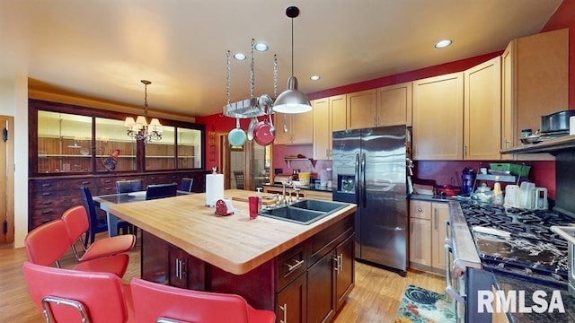 kitchen featuring stainless steel fridge, light wood-type flooring, a kitchen island with sink, sink, and an inviting chandelier