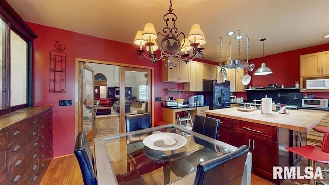 kitchen featuring a center island, a notable chandelier, pendant lighting, light hardwood / wood-style floors, and black fridge with ice dispenser