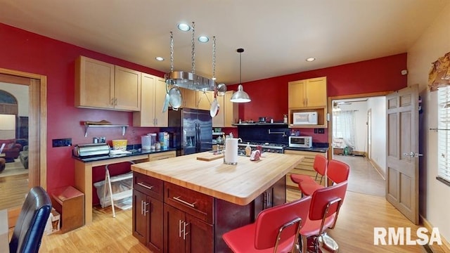 kitchen with black refrigerator with ice dispenser, hanging light fixtures, light wood-type flooring, light brown cabinetry, and a kitchen island