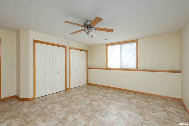 unfurnished bedroom with ceiling fan and multiple closets