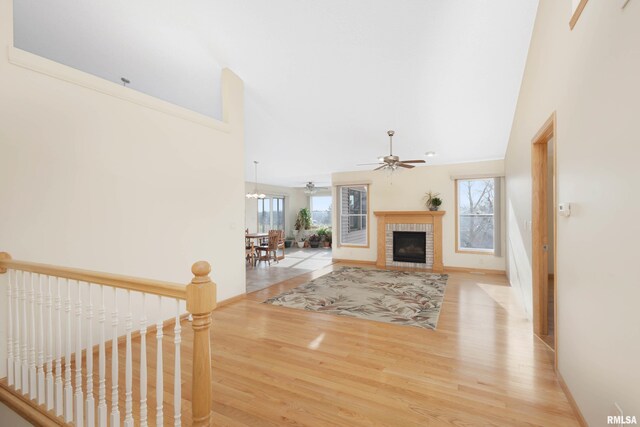 unfurnished living room featuring plenty of natural light, light wood-type flooring, ceiling fan with notable chandelier, and a brick fireplace