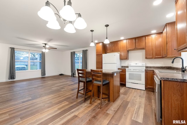 kitchen with sink, a center island, pendant lighting, white appliances, and light wood-type flooring