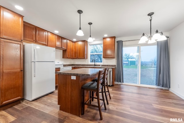 kitchen with a kitchen breakfast bar, white appliances, dark wood-type flooring, pendant lighting, and a kitchen island