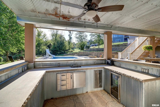 view of patio / terrace with ceiling fan, sink, beverage cooler, an outdoor kitchen, and an empty pool