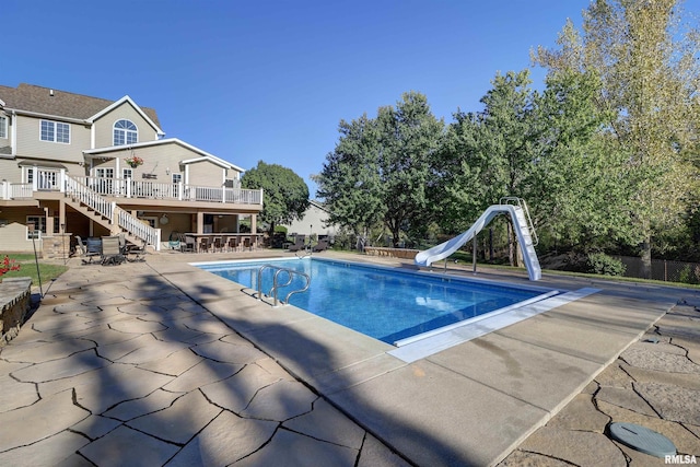 view of pool featuring exterior bar, a wooden deck, a patio area, and a water slide