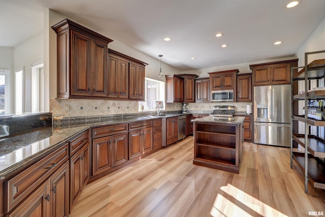 kitchen featuring pendant lighting, decorative backsplash, dark stone countertops, appliances with stainless steel finishes, and light hardwood / wood-style floors