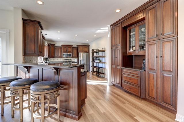 kitchen with stainless steel appliances, a kitchen breakfast bar, kitchen peninsula, decorative backsplash, and light wood-type flooring