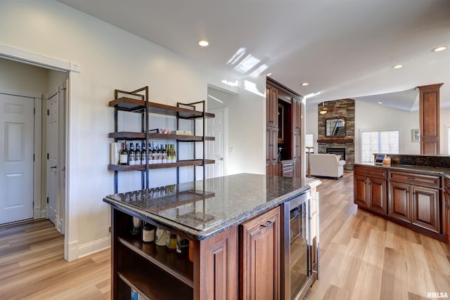 kitchen featuring a center island, dark stone counters, wine cooler, vaulted ceiling, and a fireplace