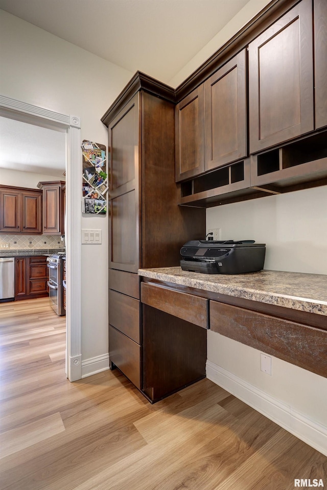 kitchen featuring appliances with stainless steel finishes, light wood-type flooring, backsplash, dark brown cabinetry, and built in desk