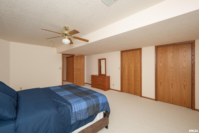 carpeted bedroom featuring a textured ceiling, two closets, and ceiling fan