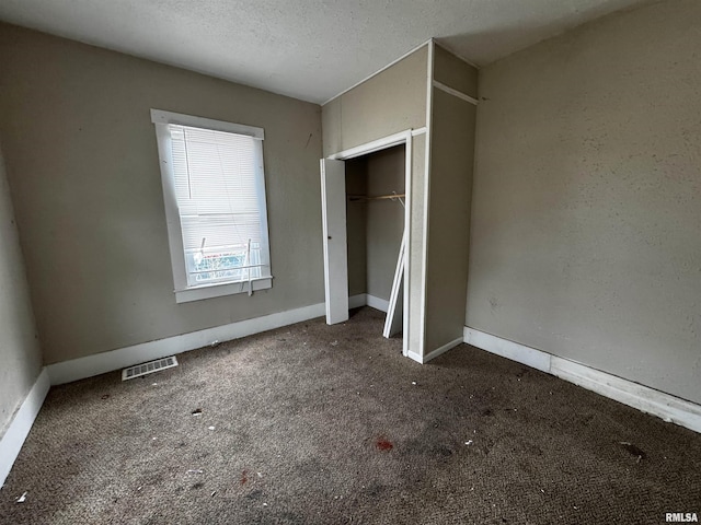 unfurnished bedroom with a closet, a textured ceiling, and dark colored carpet