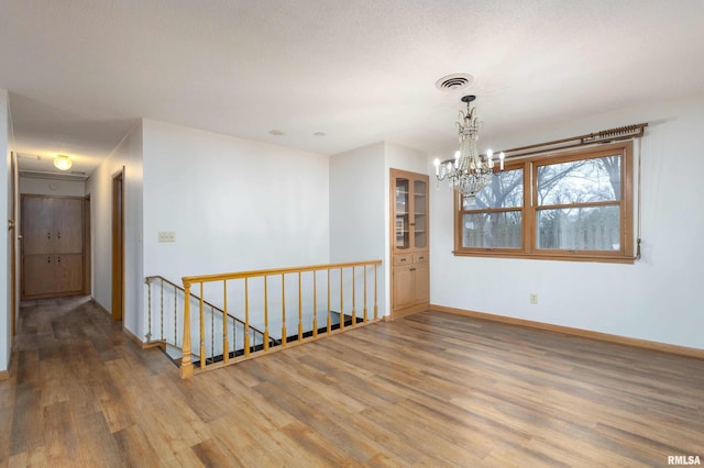 empty room featuring a notable chandelier, wood finished floors, visible vents, and baseboards