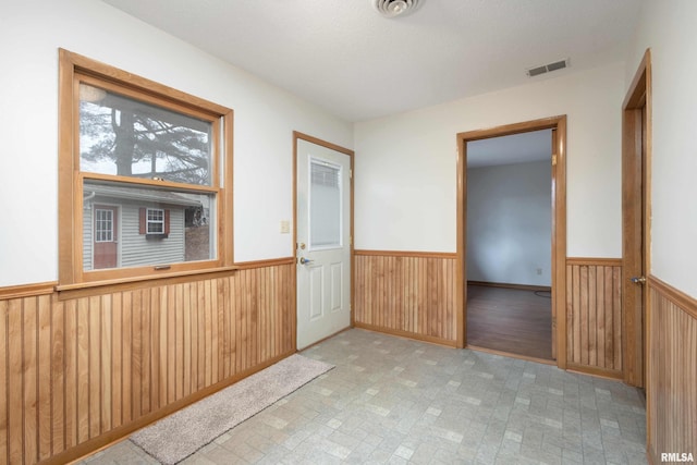 empty room featuring visible vents, wooden walls, and wainscoting