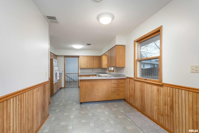 kitchen featuring wooden walls, visible vents, a peninsula, light countertops, and wainscoting