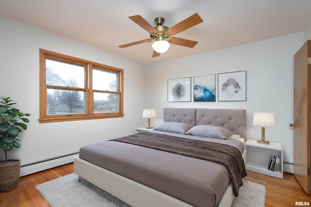 bedroom with light wood-style flooring, a baseboard heating unit, ceiling fan, and a baseboard radiator