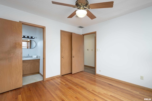 unfurnished bedroom with baseboards, visible vents, light wood-style flooring, a sink, and a textured ceiling