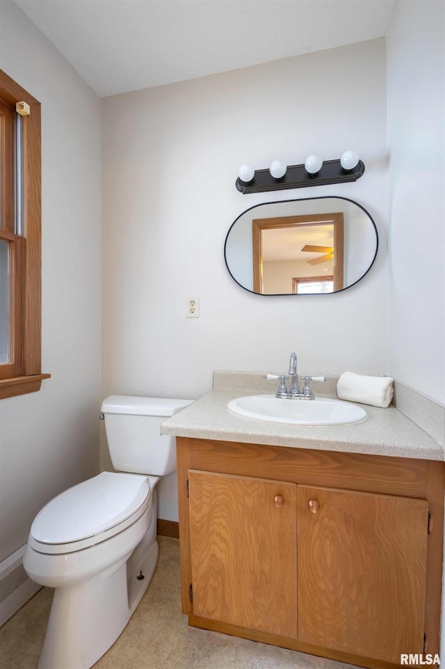 half bath with baseboards, toilet, baseboard heating, and vanity