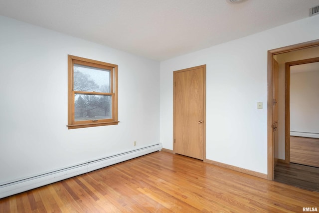 spare room featuring a baseboard heating unit, baseboards, visible vents, and light wood finished floors