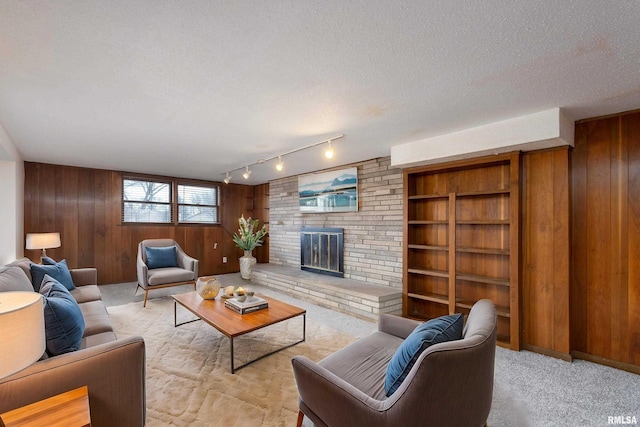 living room with light carpet, a textured ceiling, wood walls, rail lighting, and a brick fireplace