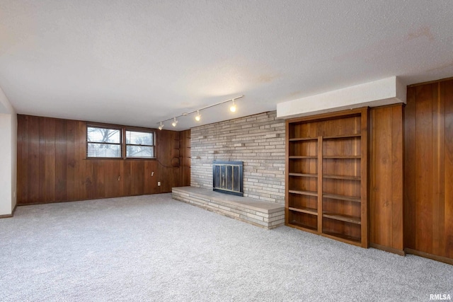 unfurnished living room with a fireplace, track lighting, wood walls, a textured ceiling, and carpet flooring