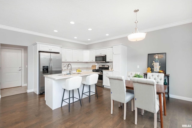 kitchen featuring dark wood-type flooring, pendant lighting, a center island with sink, white cabinets, and appliances with stainless steel finishes