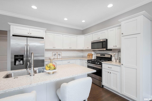 kitchen with light stone countertops, dark hardwood / wood-style flooring, ornamental molding, stainless steel appliances, and white cabinetry