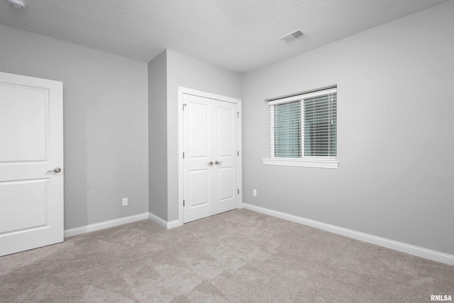 unfurnished bedroom with light colored carpet, a textured ceiling, and a closet