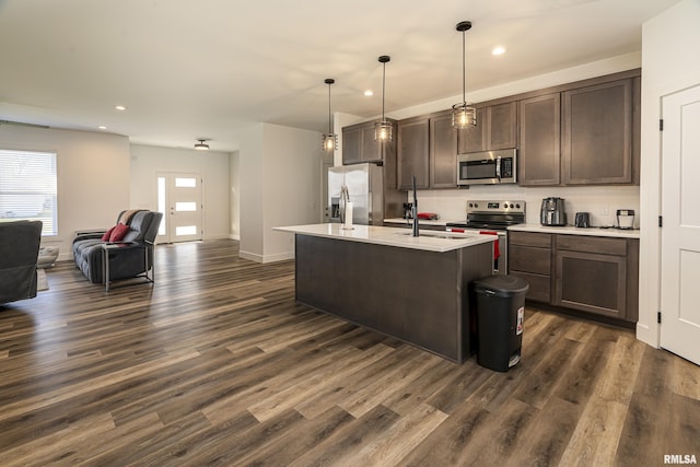 kitchen featuring dark brown cabinetry, dark hardwood / wood-style floors, an island with sink, decorative light fixtures, and appliances with stainless steel finishes