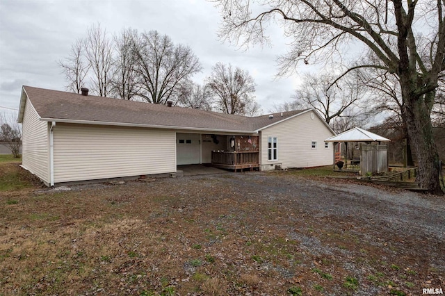 view of front of house with a garage, a deck, dirt driveway, and a shingled roof