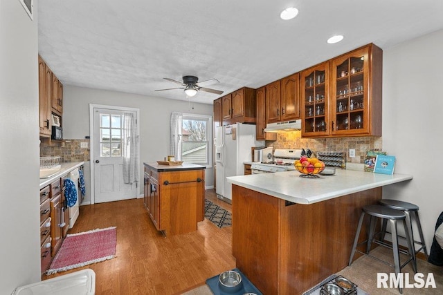 kitchen with white appliances, hardwood / wood-style floors, ceiling fan, tasteful backsplash, and kitchen peninsula