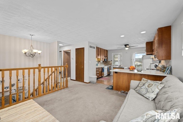 kitchen with white refrigerator, light carpet, kitchen peninsula, ceiling fan with notable chandelier, and pendant lighting