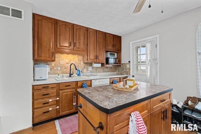 kitchen featuring sink, light wood-type flooring, ceiling fan, decorative backsplash, and a kitchen island