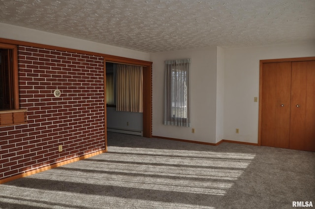 carpeted spare room with a textured ceiling, baseboard heating, and brick wall