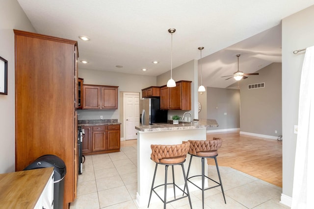 kitchen featuring kitchen peninsula, stainless steel refrigerator with ice dispenser, light tile patterned floors, hanging light fixtures, and a breakfast bar area