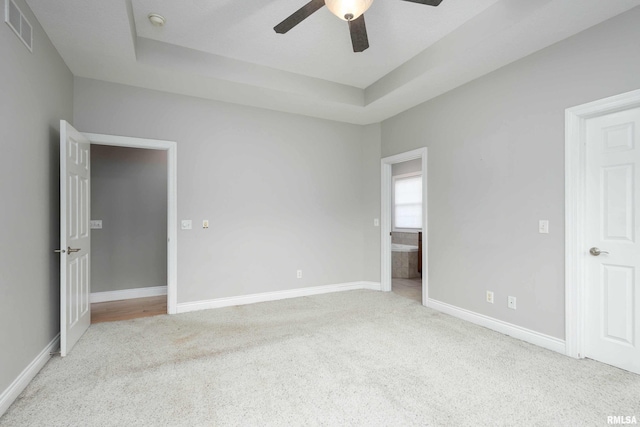 unfurnished bedroom with a tray ceiling, ceiling fan, and light colored carpet