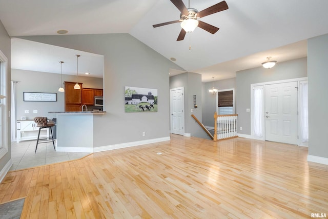 unfurnished living room with ceiling fan with notable chandelier, light hardwood / wood-style floors, sink, and high vaulted ceiling