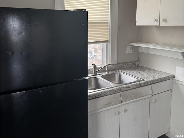 kitchen with white cabinetry, black fridge, and sink