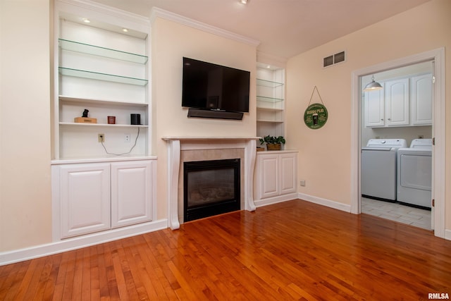 unfurnished living room featuring built in shelves, light hardwood / wood-style floors, a tiled fireplace, and washing machine and clothes dryer