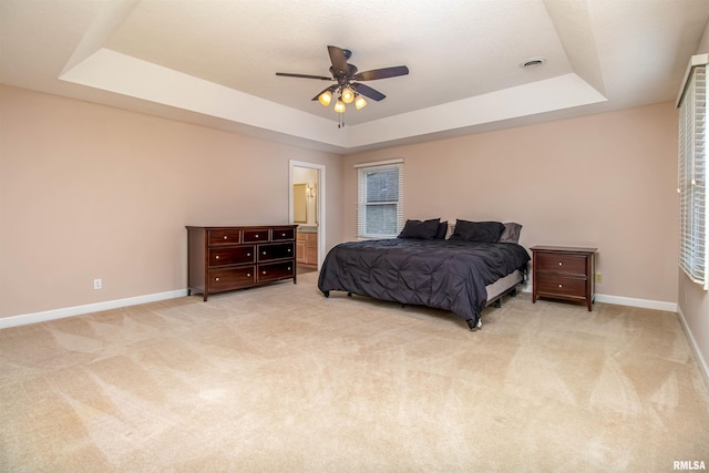 bedroom featuring a tray ceiling, connected bathroom, ceiling fan, and light colored carpet