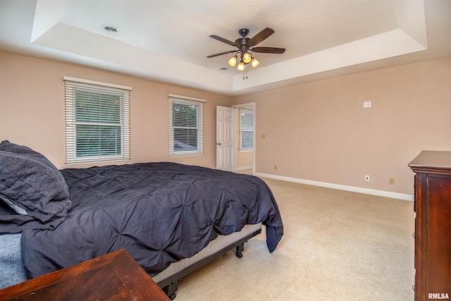 carpeted bedroom featuring a tray ceiling and ceiling fan