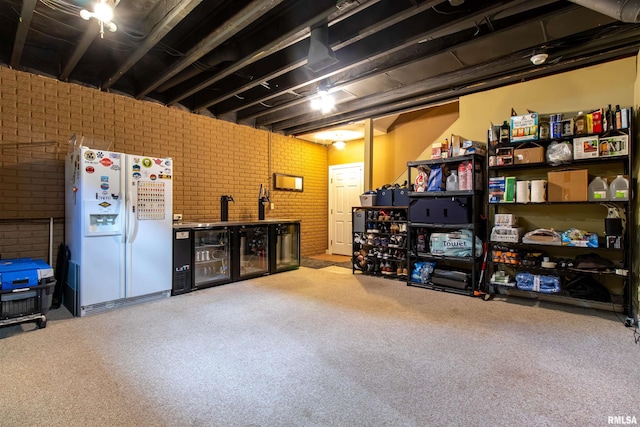 basement featuring white fridge with ice dispenser, beverage cooler, and brick wall