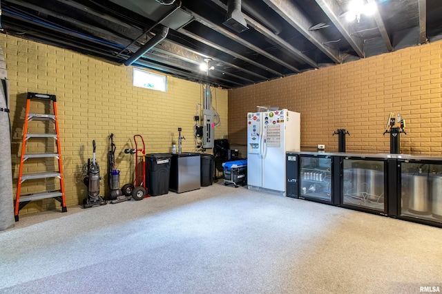 basement featuring white fridge, brick wall, and beverage cooler