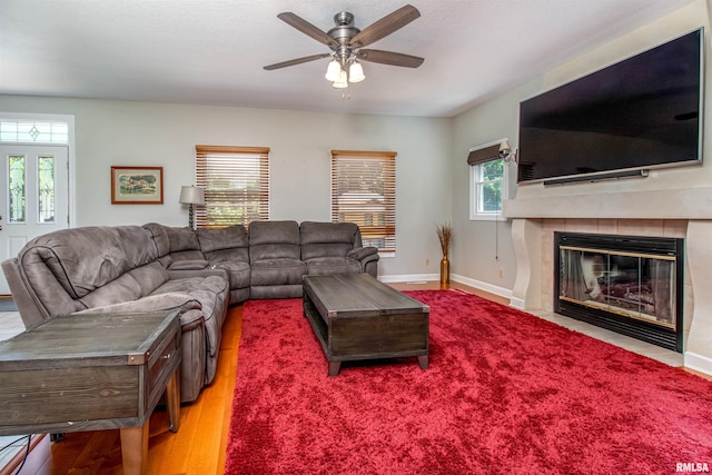 living room with a fireplace, light wood-type flooring, ceiling fan, and a healthy amount of sunlight